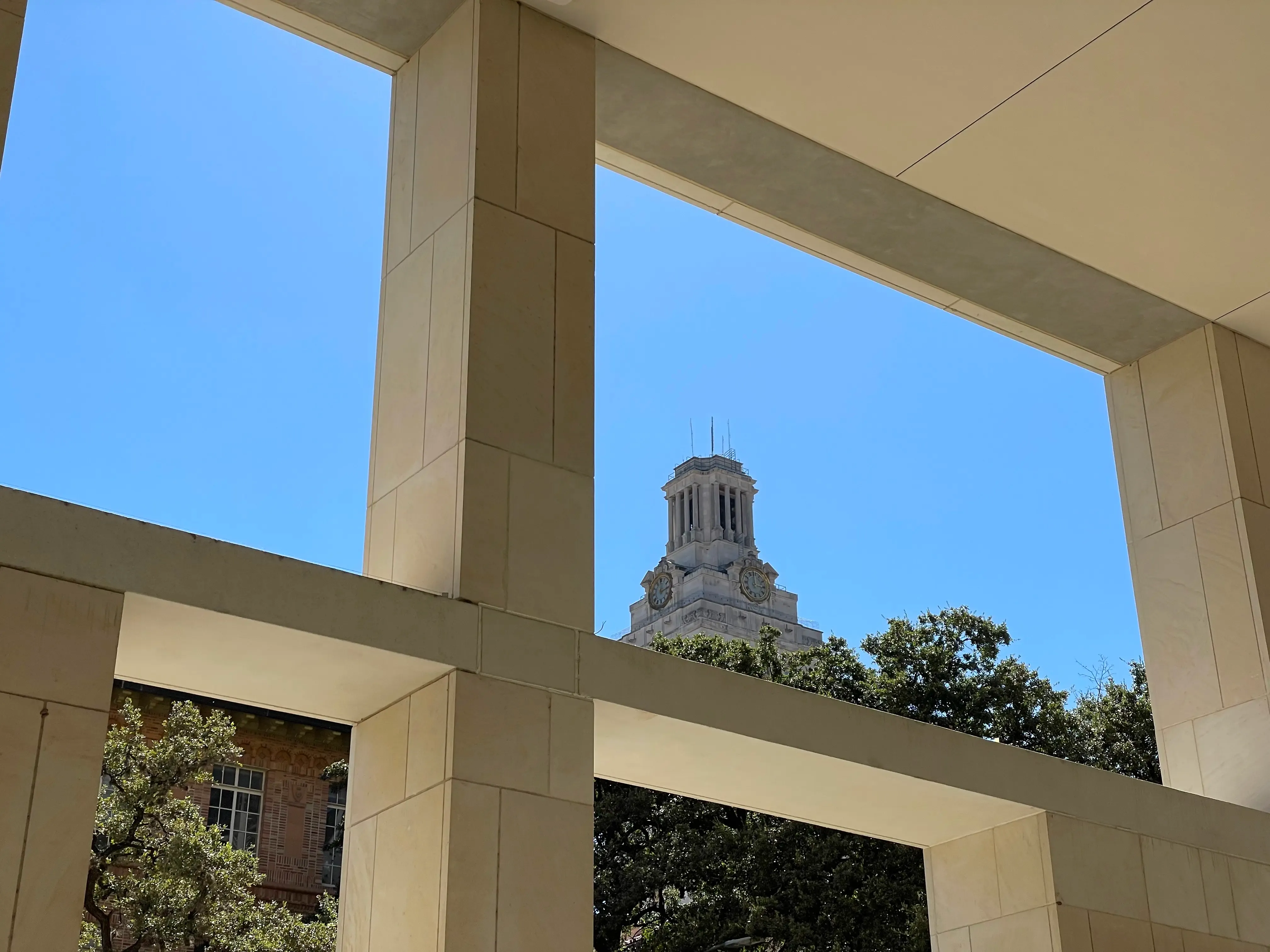 Blue sky looking at the UT Tower framed by a building.