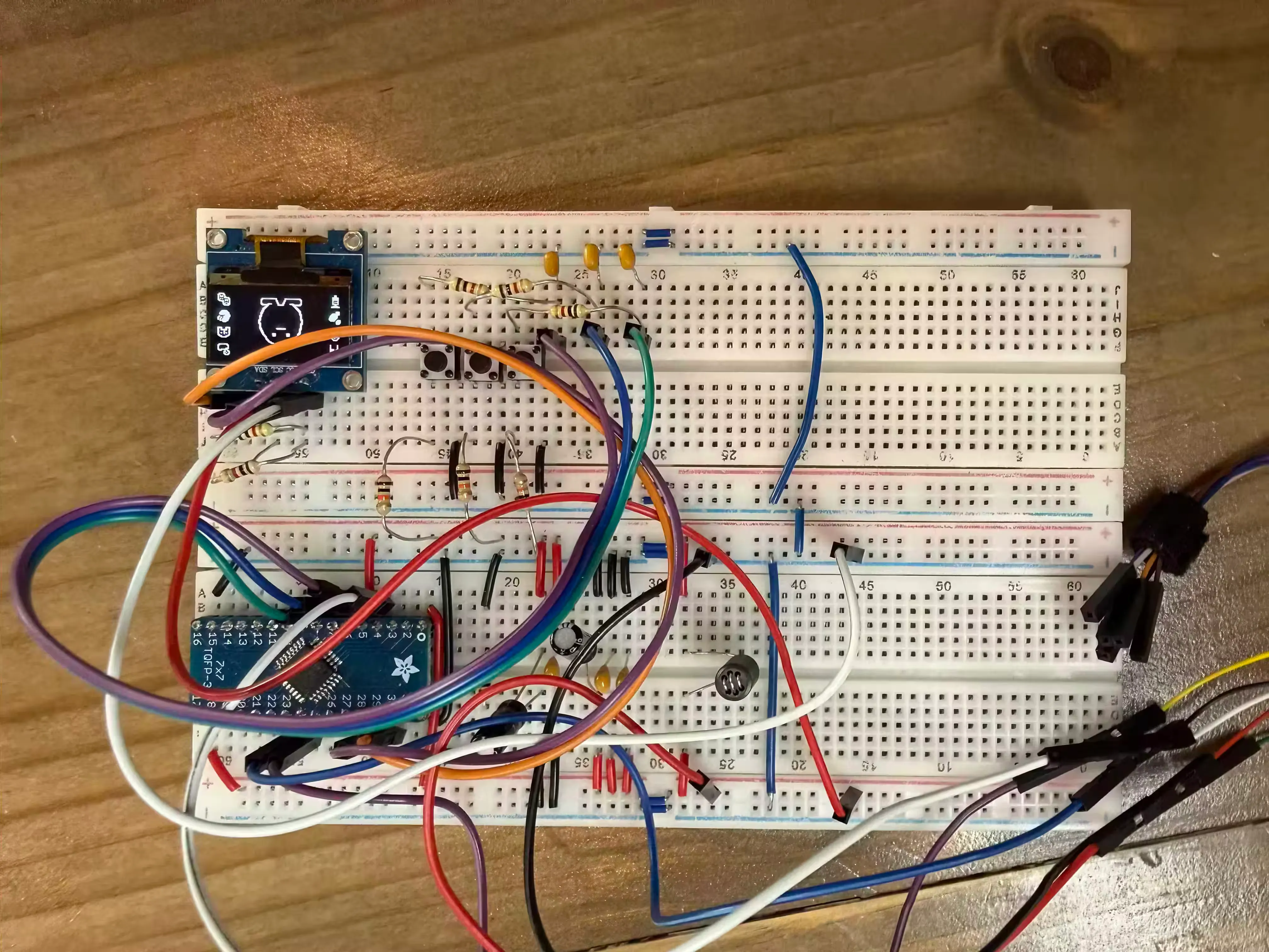 Breadboard with a microcontroller hooked
up to a set of 3 buttons and a small screen. On the screen is a set of icons and
a small digital creature.